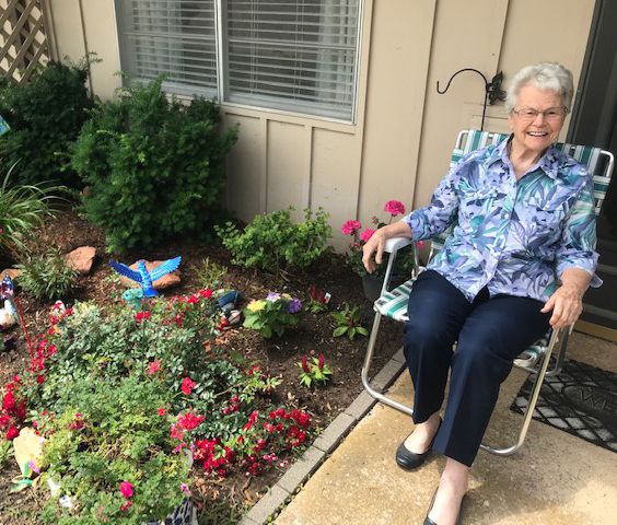 An elderly woman sitting in a chair next to a colorful garden.
