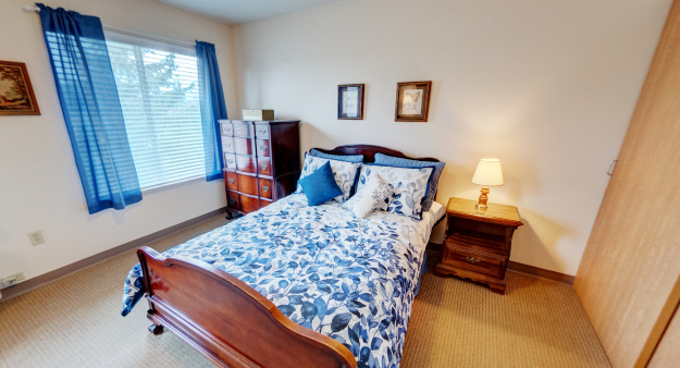 A cozy bedroom with a wooden bed, floral bedding, and a warm-lit lamp.