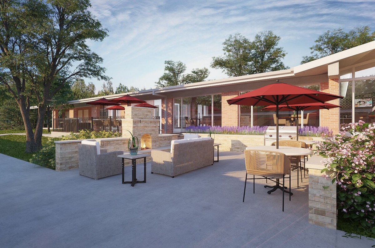 A modern outdoor patio with comfortable seating and sun umbrellas, set against a backdrop of trees.