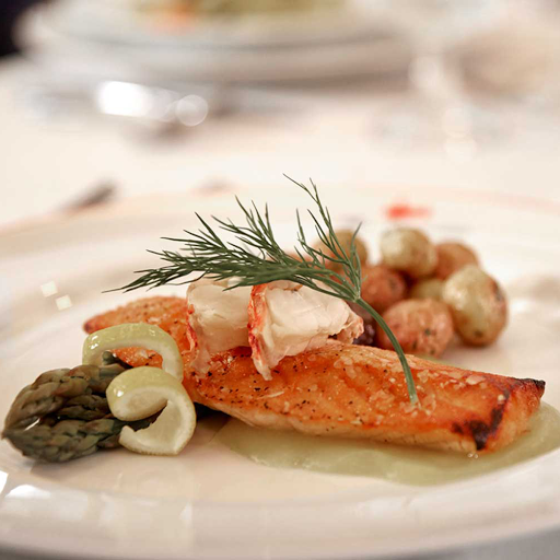 A beautifully plated dish featuring salmon, garnished with fresh herbs and accompanied by small vegetables.