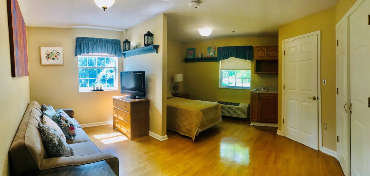 A cozy bedroom with a wooden floor, featuring a bed, dresser, TV, and large window.