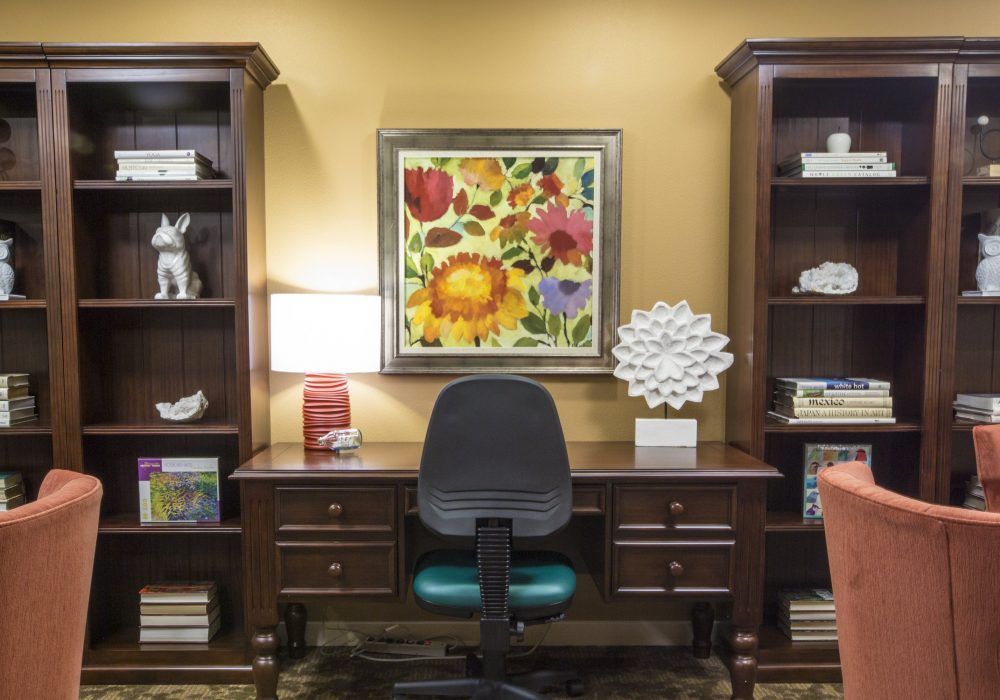A well-organized office with a desk and chair, flanked by bookshelves and decorated with colorful artwork.