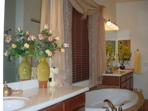 A beautifully decorated bathroom featuring floral arrangements, elegant curtains, and a spacious vanity area.
