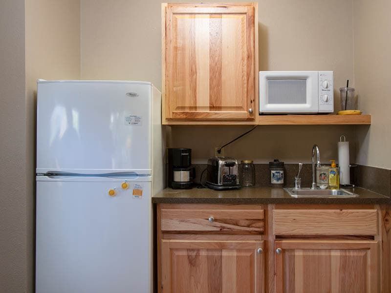 A compact kitchen area with a refrigerator, microwave, coffee maker, and sink.