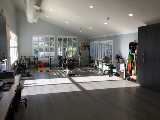A well-lit gym space with multiple exercise equipment and large windows.