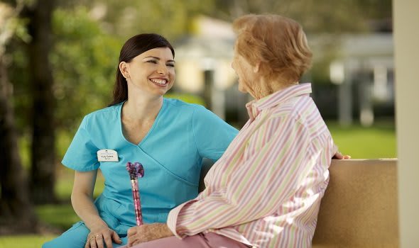 A nurse and an elderly woman smiling and conversing outdoors.