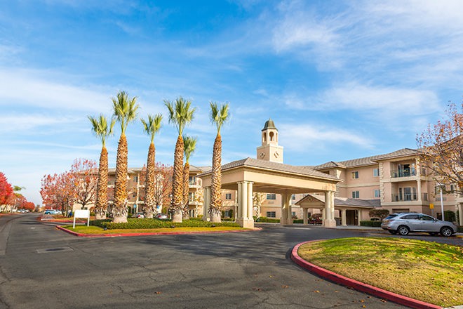 A grand entrance to a building with palm trees lining the driveway under a clear blue sky.