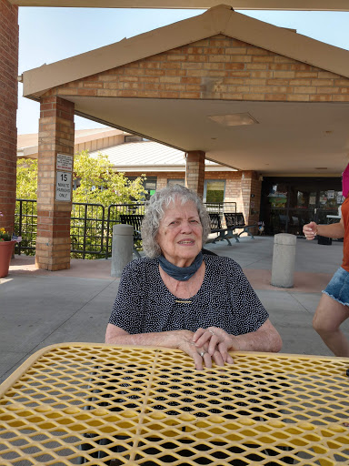 An elderly woman enjoying a sunny day outdoors, seated at a yellow table.