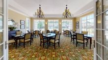 An elegant dining room with several tables and chairs, featuring chandeliers and large windows.