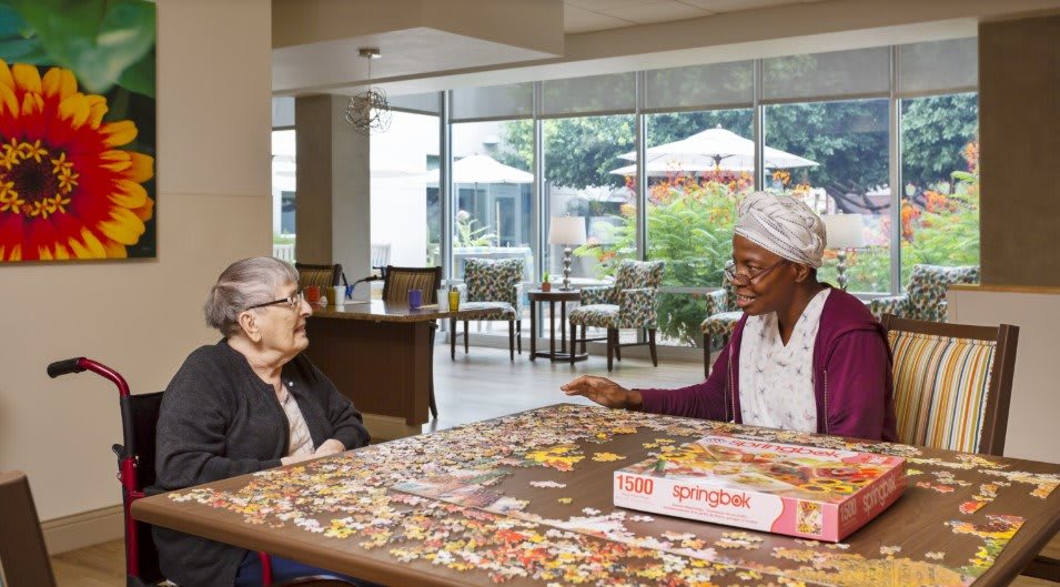 Two seniors enjoying a puzzle together in a bright and welcoming community space.