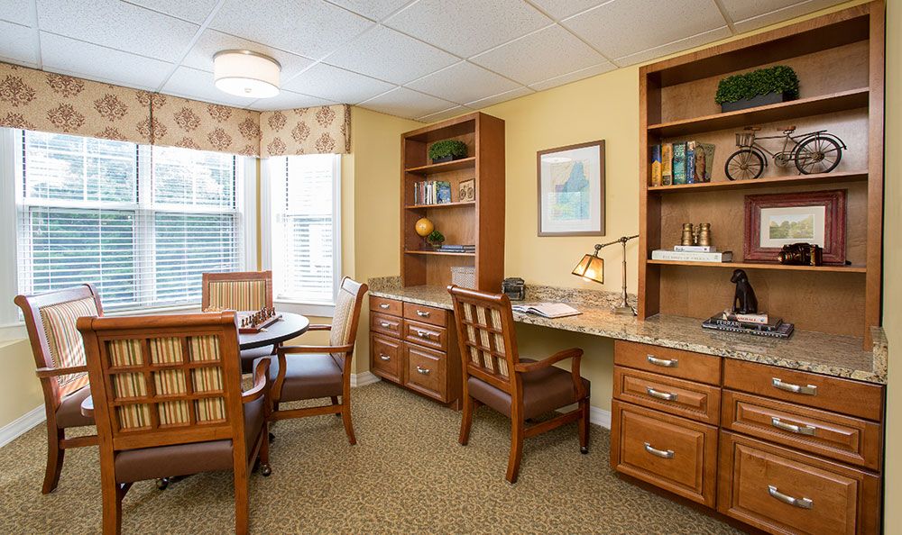 A cozy office space with a desk, chairs, bookshelves, and large windows providing natural light.