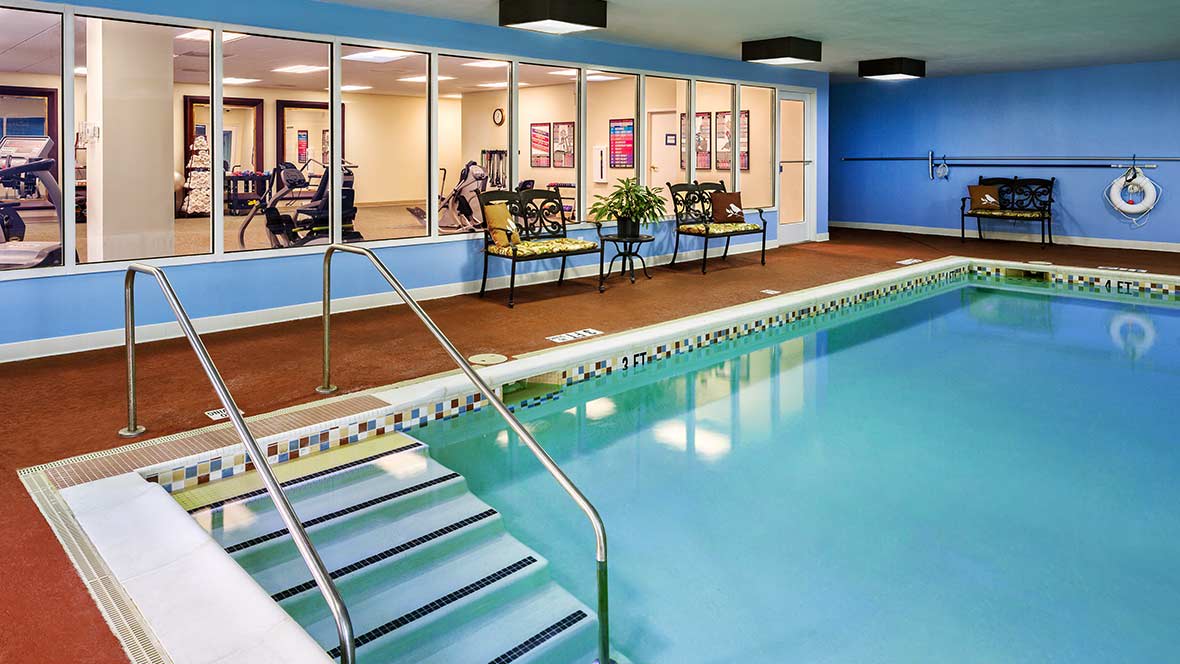 An indoor swimming pool adjacent to a fitness center with gym equipment and blue accent walls.