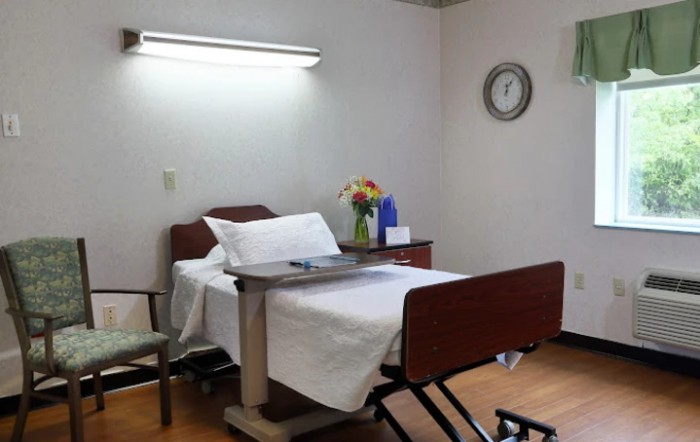 A hospital room with a bed, bedside table, and flowers.