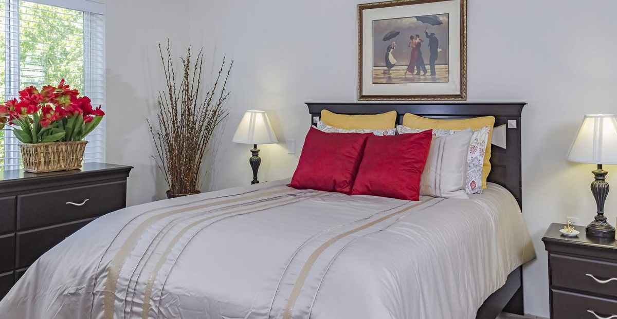 A neatly made bed with red pillows, a bedside lamp, and artwork above the headboard in a cozy bedroom.