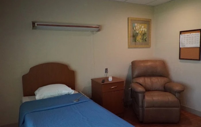 A simple hospital room with a bed, armchair, and wall art.