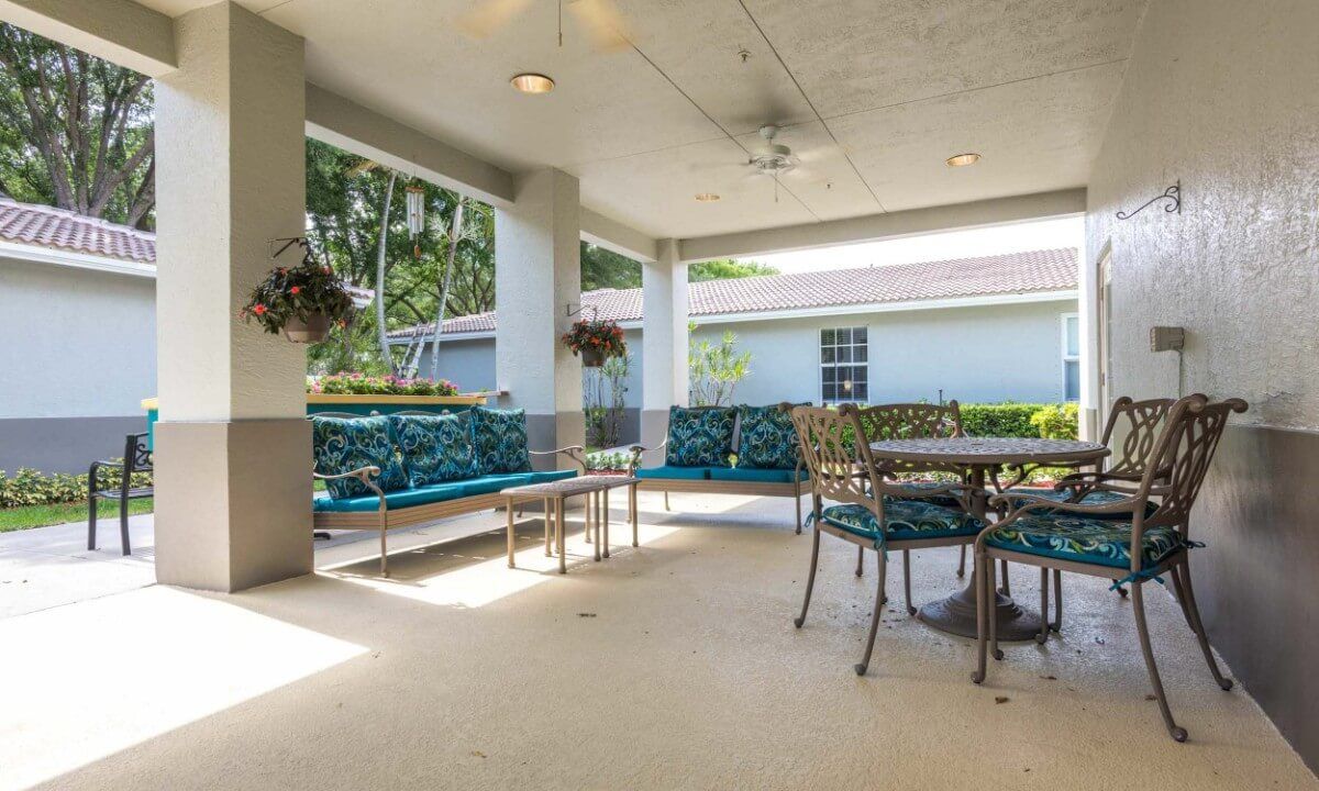 A spacious covered patio with comfortable seating and a dining table, surrounded by lush greenery.