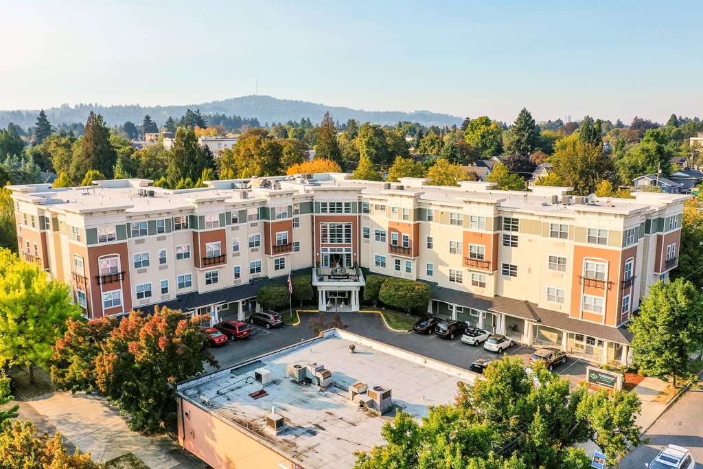 Aerial view of a residential apartment complex surrounded by trees and a parking area.