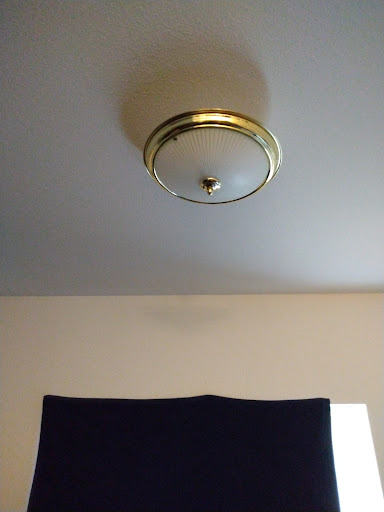 A view of a ceiling light fixture above a window with a dark curtain.