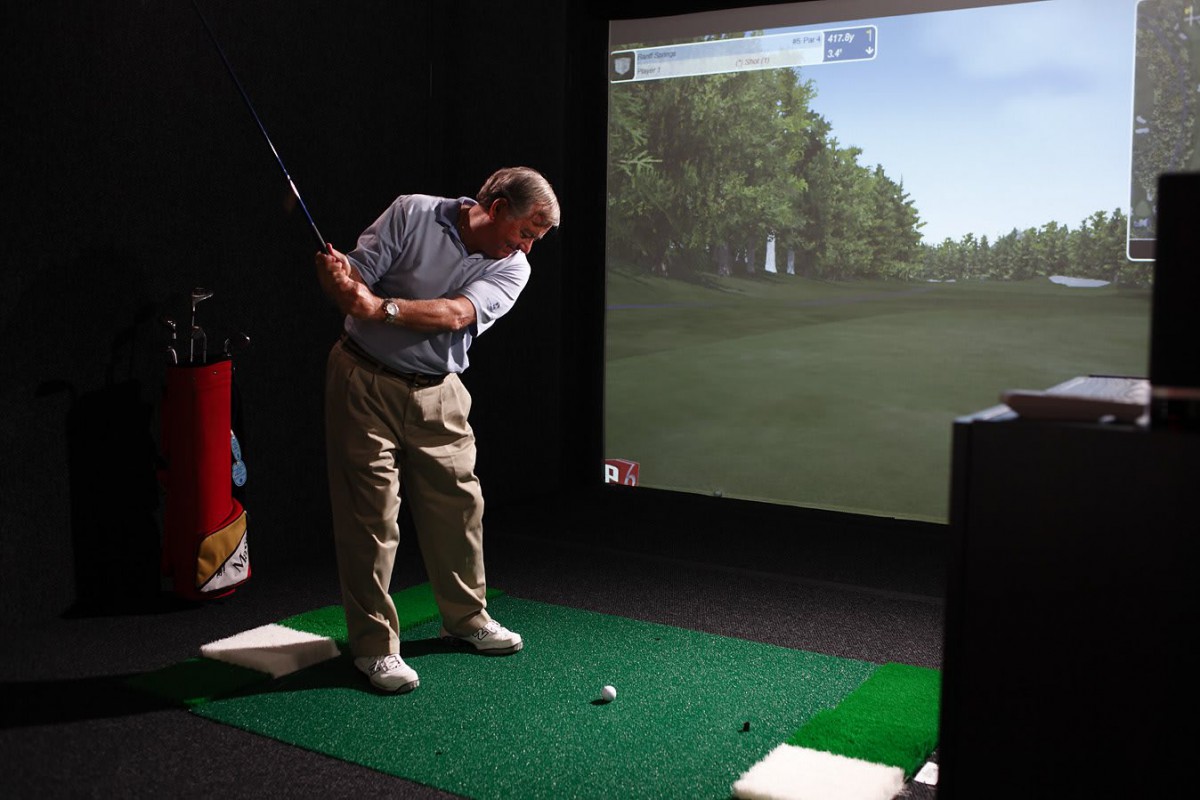 A person practicing golf using an indoor simulator.