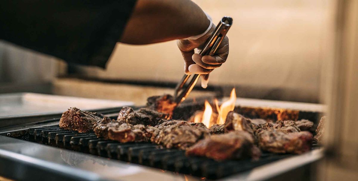 A person grilling meat over an open flame using tongs.
