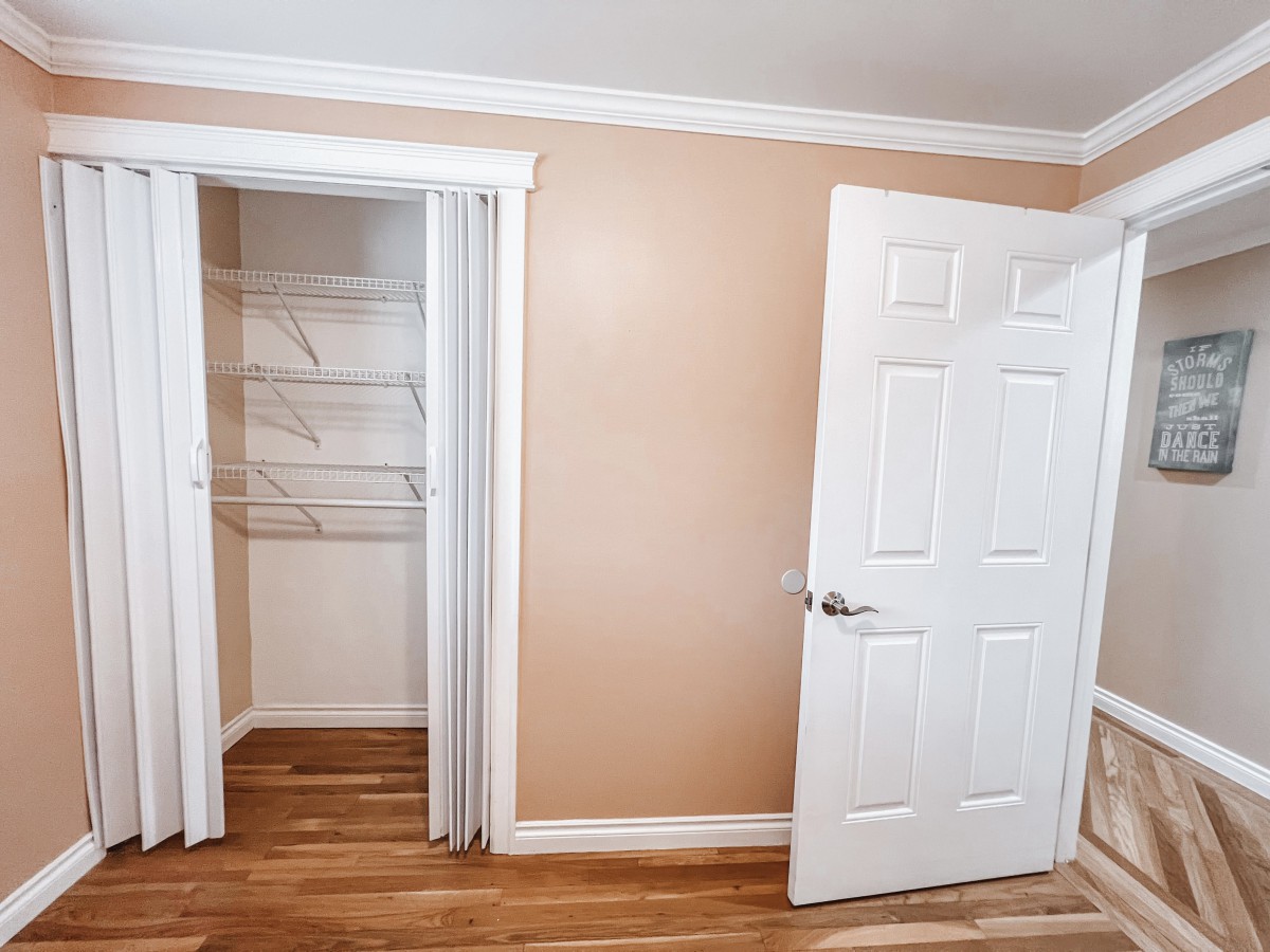 An empty room with a closet and open door, featuring wood flooring and beige walls.