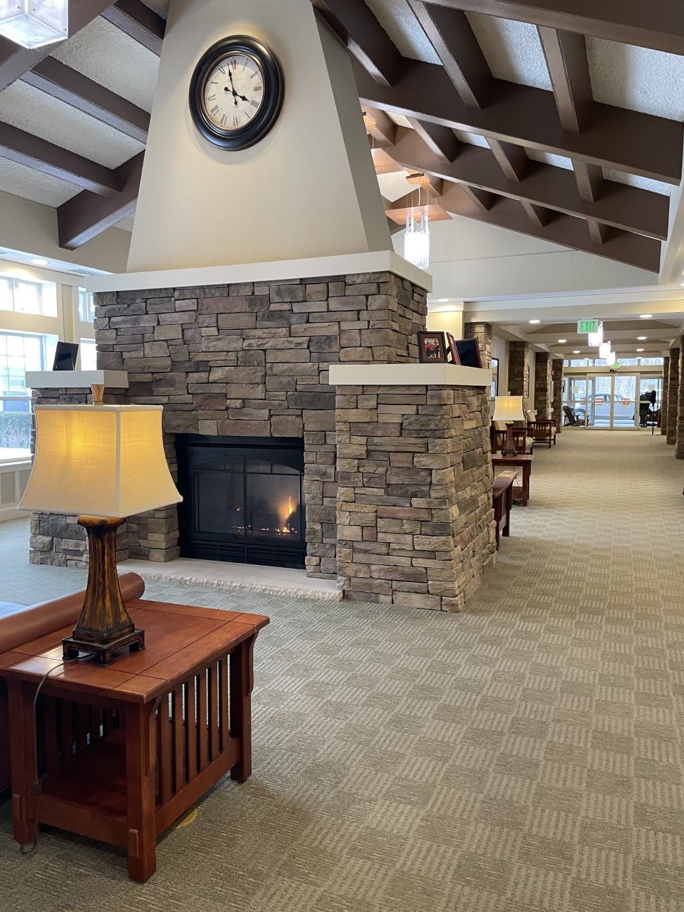 A cozy interior hallway featuring a stone fireplace, wooden furniture, and ceiling beams.