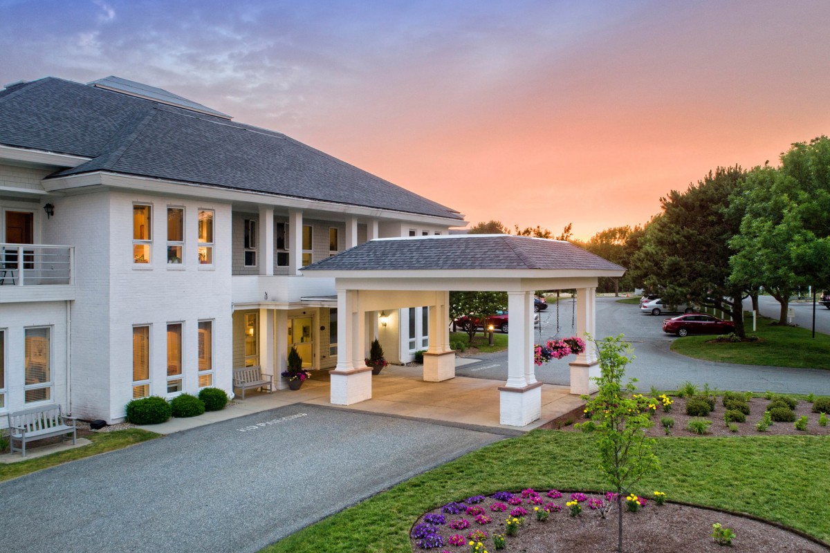A scenic view of a building entrance at sunset with a landscaped driveway.