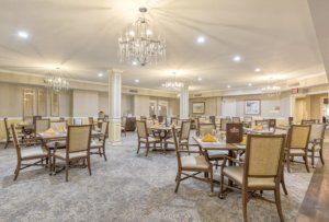 A spacious, elegantly decorated dining room featuring multiple tables and chairs under chandeliers.