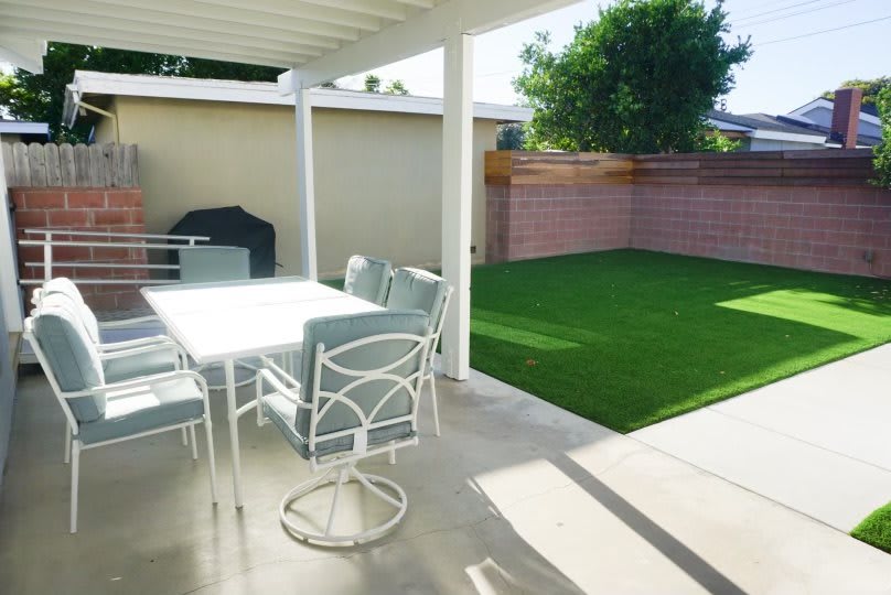 A sunny backyard patio with a table, chairs, grill, and a well-maintained lawn.