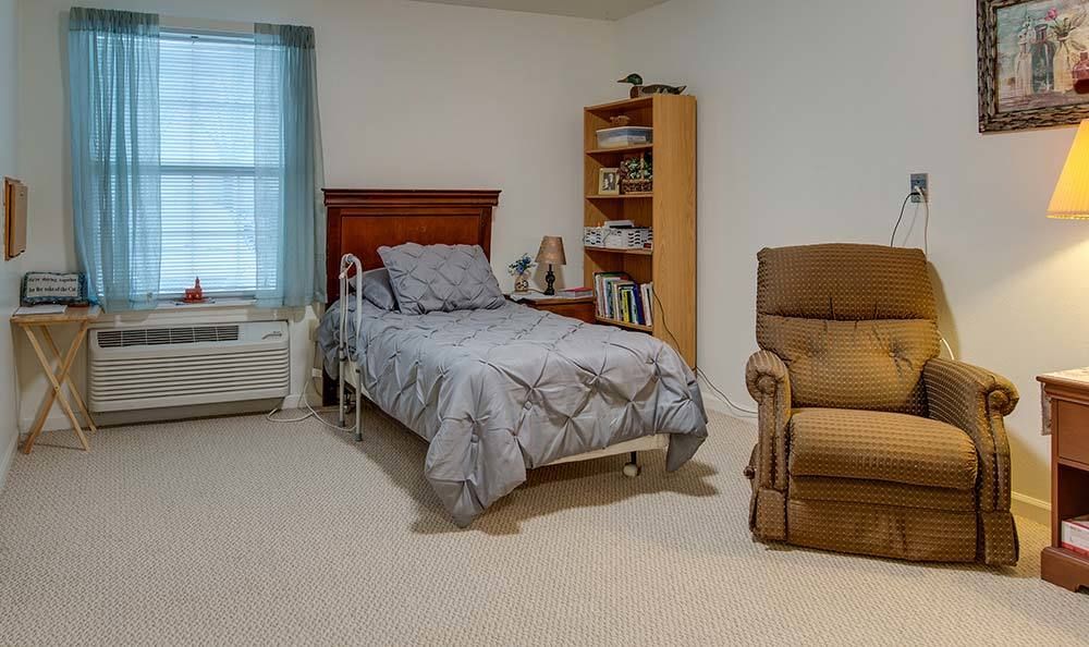 A cozy bedroom with a single bed, wooden bookshelf, and a comfortable armchair.