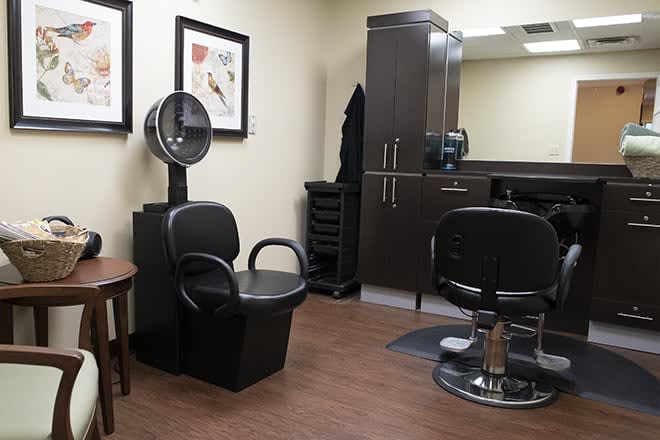 A well-equipped hair salon with chairs, a hair dryer, and a large mirror.
