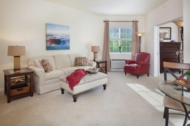 A cozy living room featuring a beige sofa, red armchair, and a large window providing natural light.