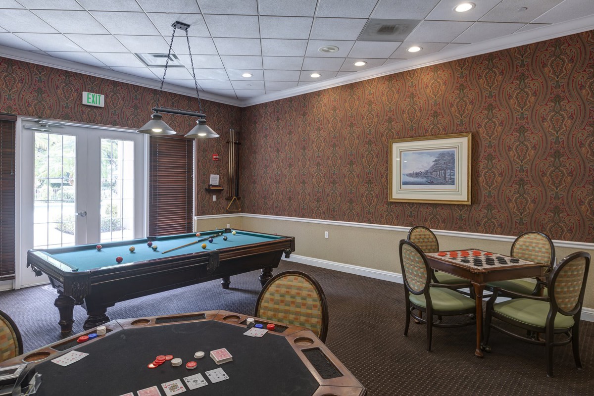 A cozy game room featuring a pool table and card tables with comfortable seating.