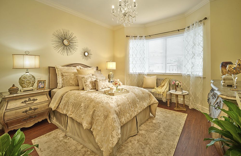 A luxurious and elegantly decorated bedroom featuring a plush bed, chandelier, and warm lighting.