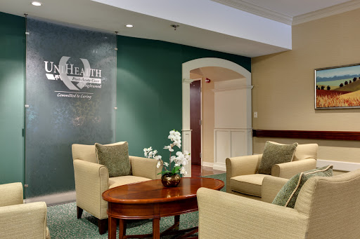 A cozy lobby seating area featuring comfortable chairs and a wooden table, accented by a green wall and decorative plants.