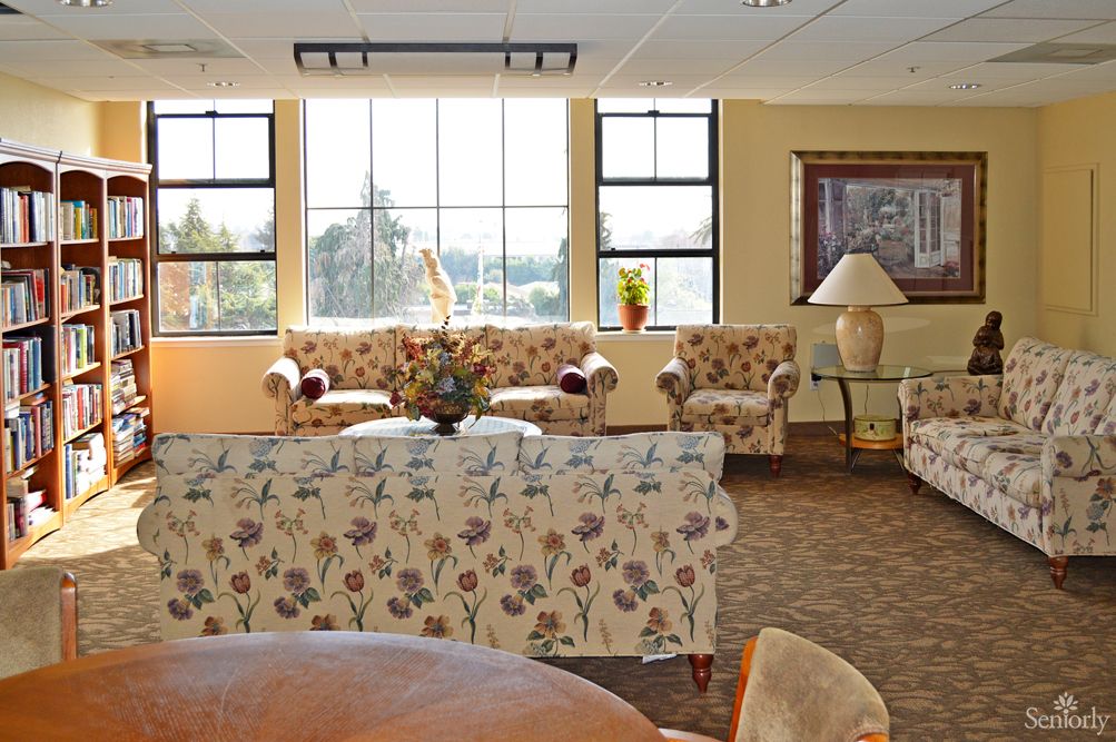 A cozy living room with floral patterned sofas, a coffee table, and large windows letting in natural light.