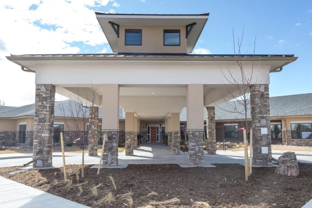 The image shows the entrance to a modern building with a covered walkway supported by stone columns.