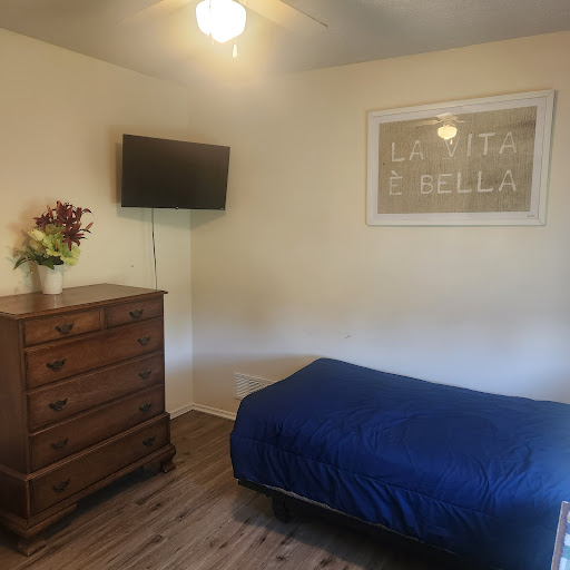 A cozy bedroom featuring a single bed with a blue blanket, a wooden dresser, and a mounted TV.