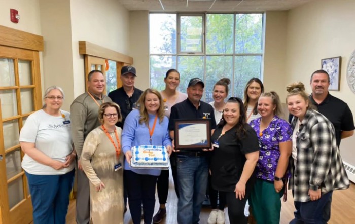 A group of individuals celebrating an achievement with an award and cake in an indoor setting.