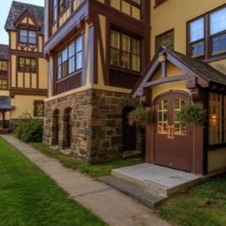 A Tudor-style building with intricate stonework and an inviting entrance surrounded by a well-maintained lawn.