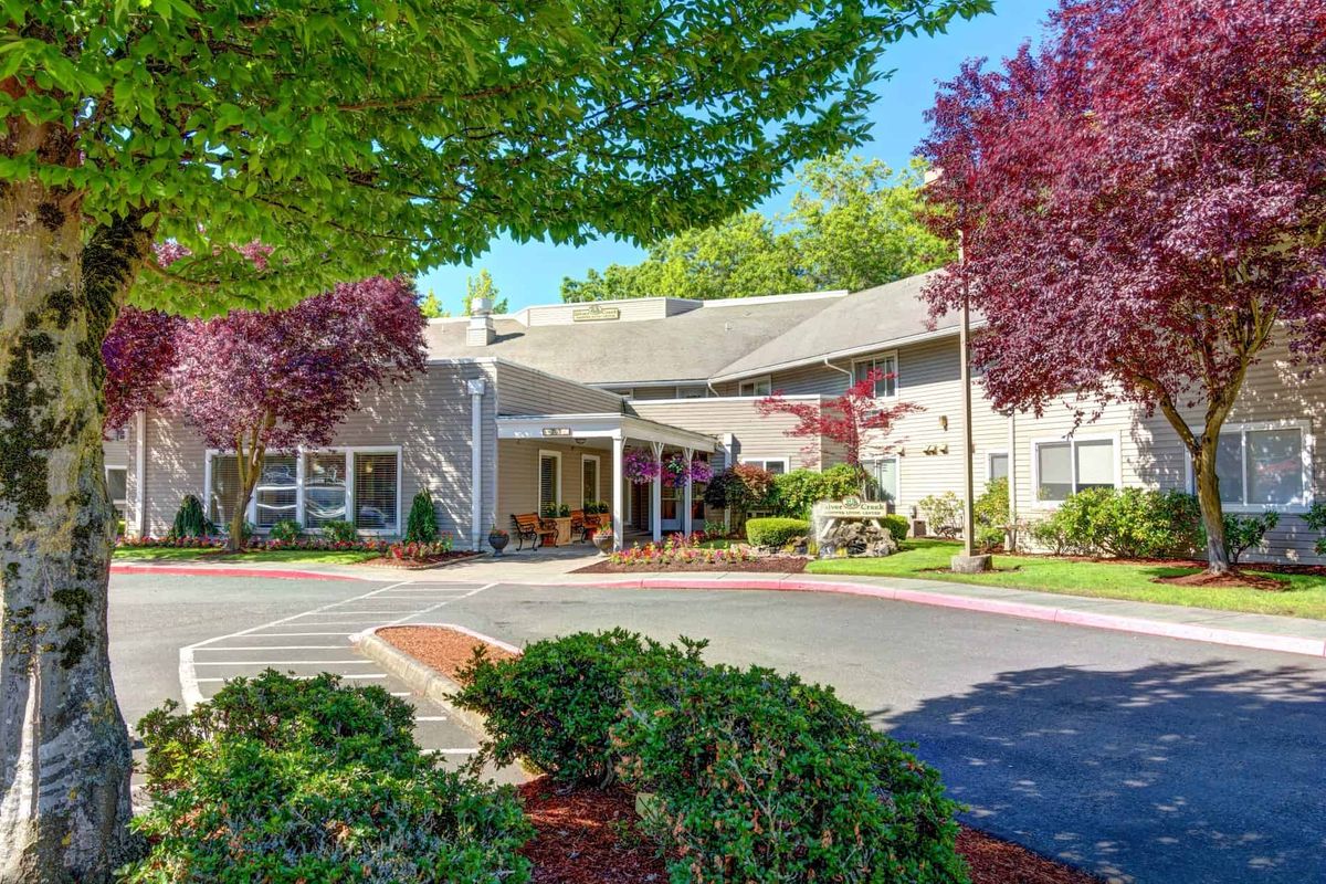 A well-maintained building entrance surrounded by lush landscaping and colorful trees on a sunny day.