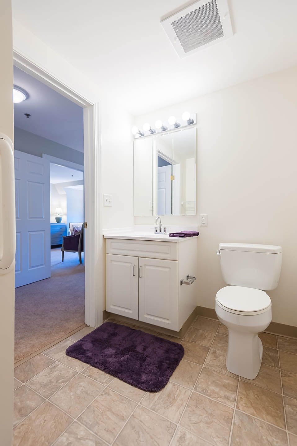 A clean and minimalistic bathroom with a sink, mirror, and toilet set on a tiled floor.