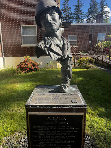 A striking bust sculpture commemorating a notable individual, set in a green outdoor space.