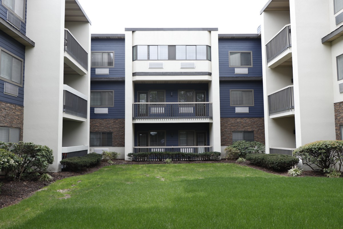 A modern apartment building with multiple balconies and a green lawn in front.
