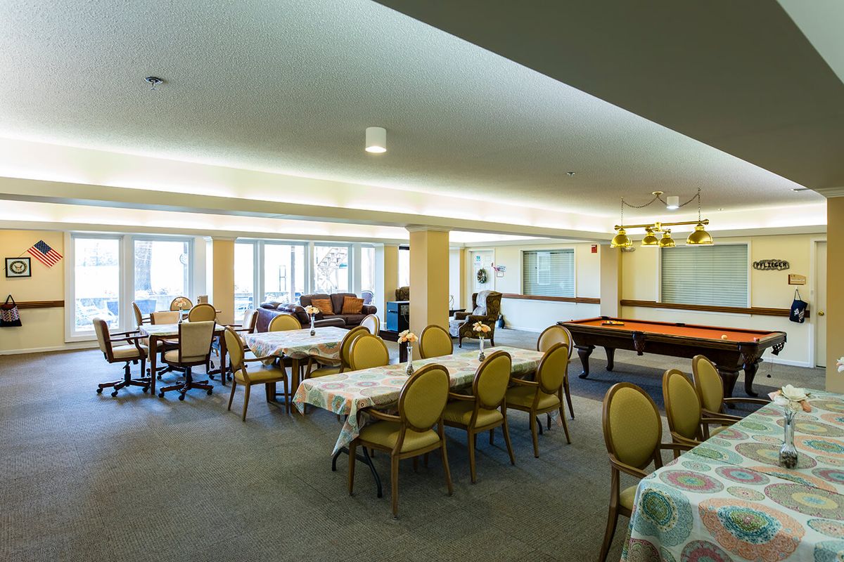 A spacious and well-lit community dining and recreational area with tables, chairs, and a pool table.