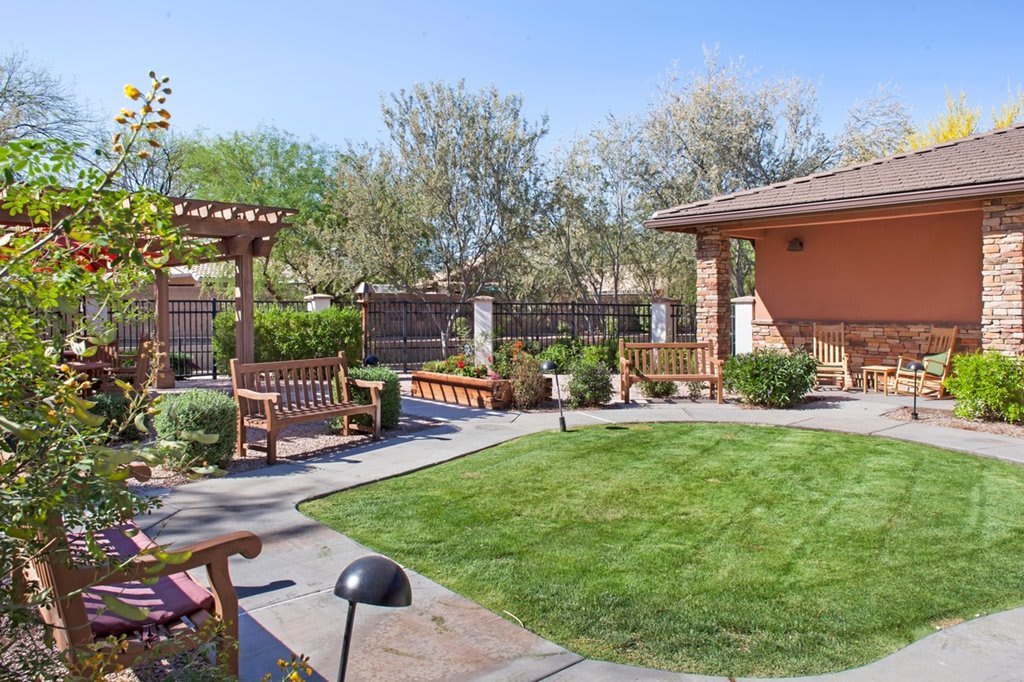 A beautifully landscaped garden featuring a pergola, lush grass, and outdoor seating.