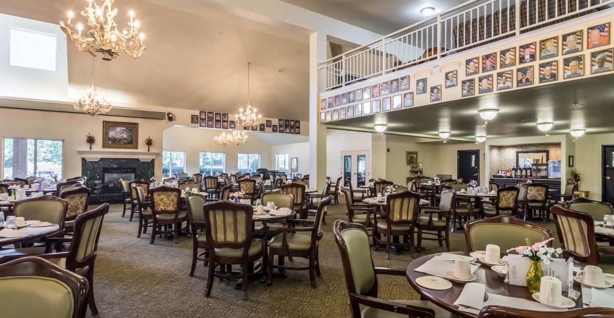 An elegant dining room with multiple tables and chairs, featuring a chandelier and balcony area.