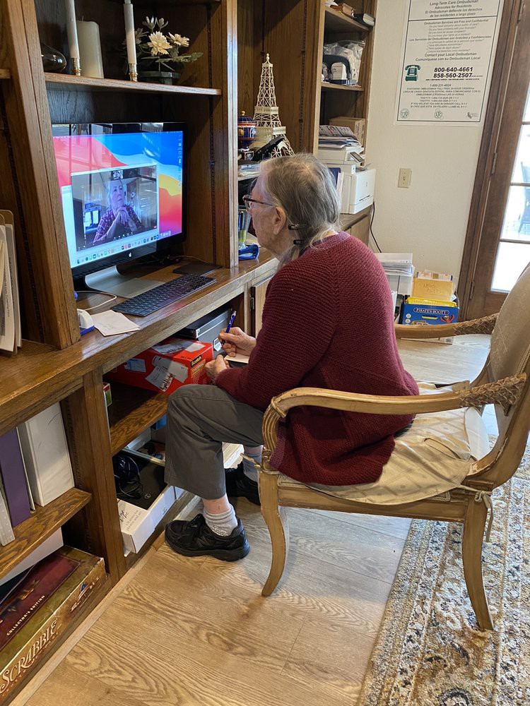 An elderly person using a computer while seated in a room with bookshelves.