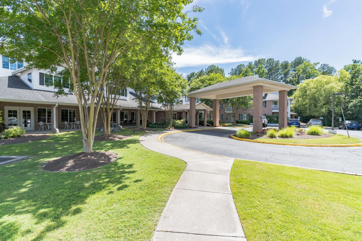 A well-maintained building entrance surrounded by green landscaping and trees on a sunny day.