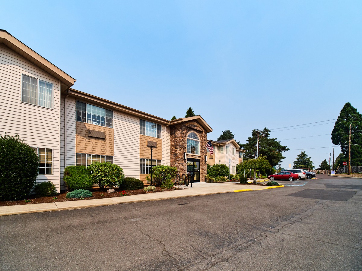 A two-story hotel building with a parking lot and landscaped entrance surrounded by trees.